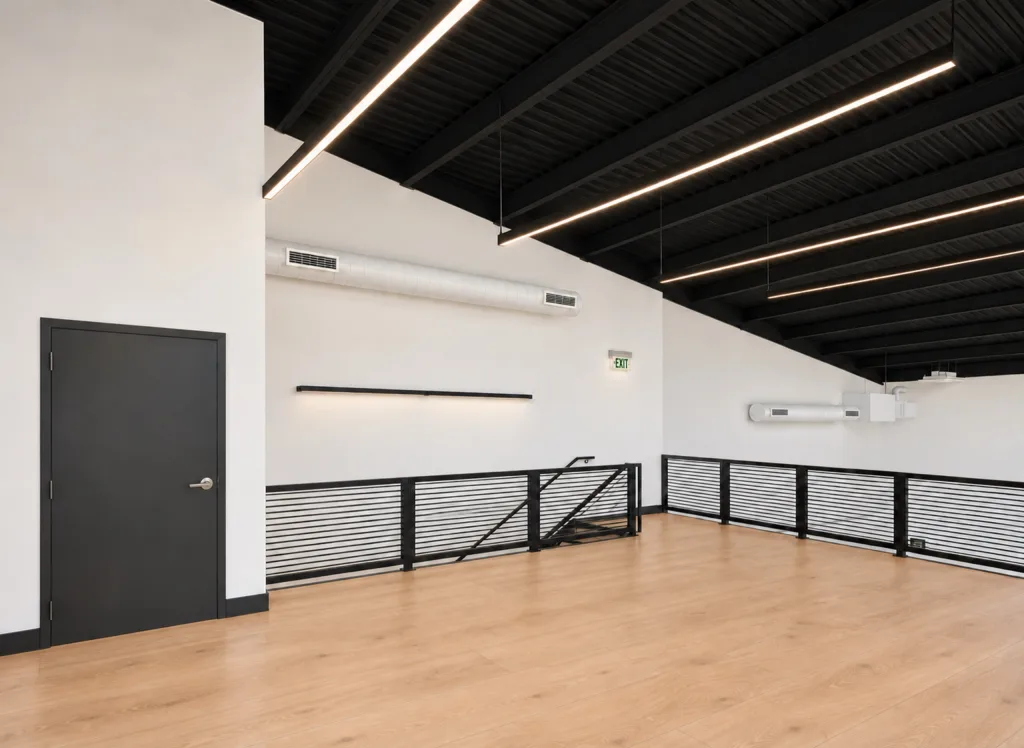 Second floor with wood-tone flooring, a sloped black ceiling, white ductwork, a door and railings over the stair