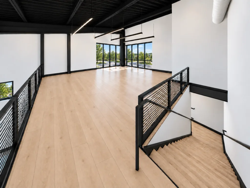 Second-floor room with wood-tone flooring, black railings, a stair leading down and windows at the far end